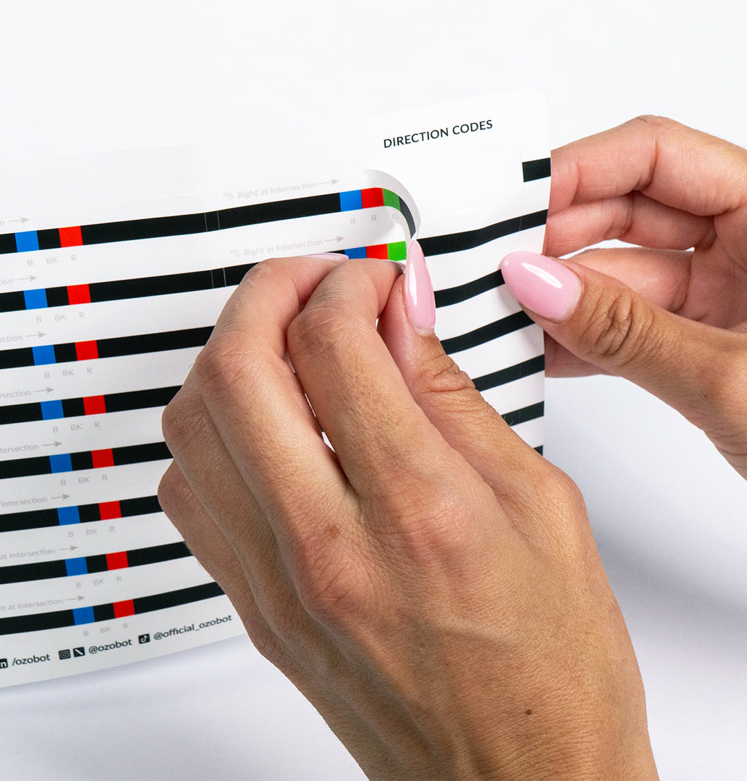 Hand peeling an Ozobot Color Code Sticker from a sheet for easy classroom and student use