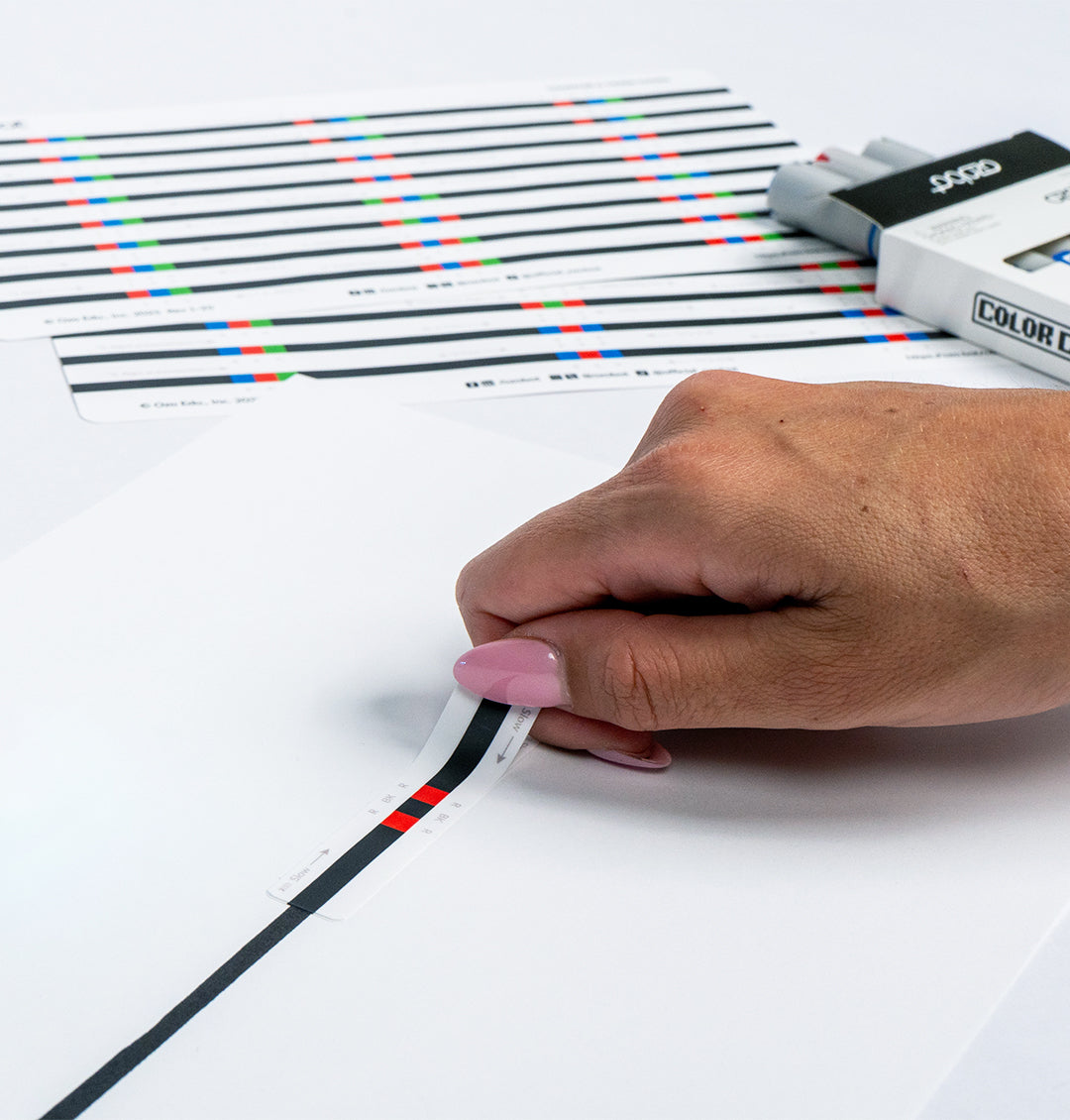 Hand applying an Ozobot Color Code Sticker to a black track line for coding activities